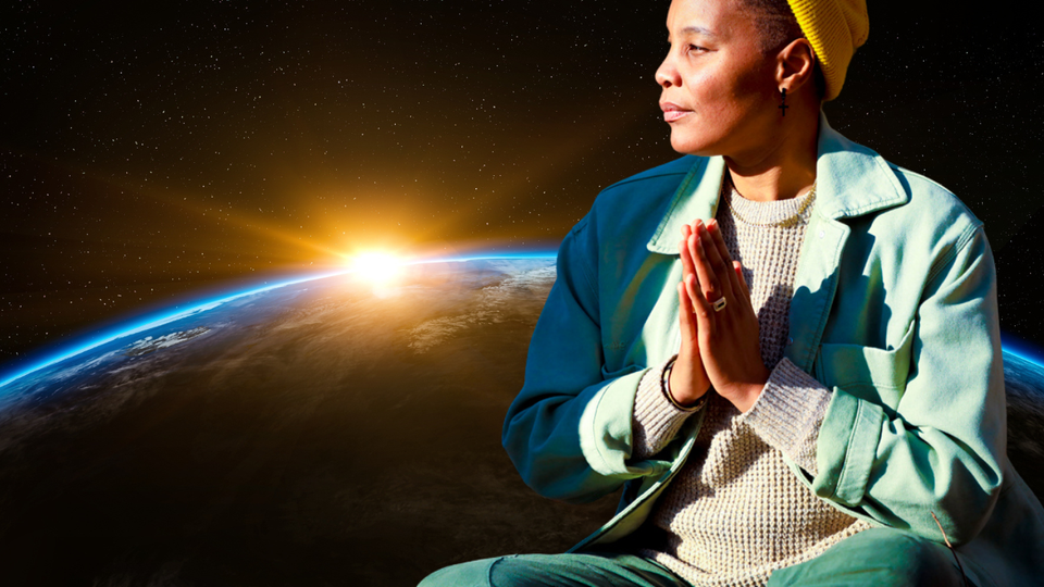 A photo of V Woods sitting hands together at heart, floating in space with the curvature of earth in the background